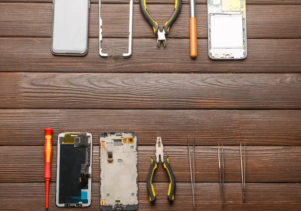 Disassembled mobile phones with technician tools on wooden background