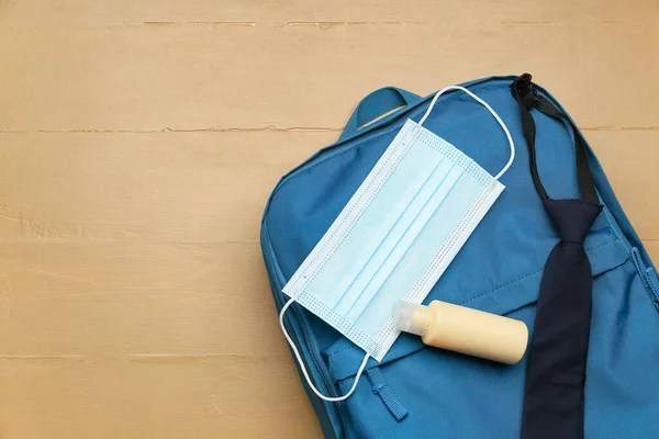 School backpack, medical mask and antiseptic on color wooden background