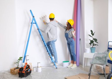 Mutlu genç çift yeni evlerinde duvar boyuyor.