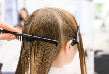 Güzellik salonunda müşterinin saçını tarayan kadın kuaför, yakın plan.