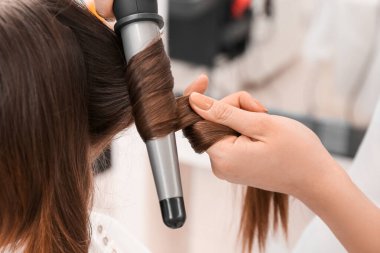 Güzellik salonunda müşterinin kıvırcık saçlı kadın kuaförü, yakın plan.