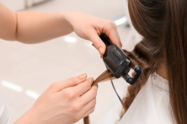 Güzellik salonunda müşterinin kıvırcık saçlı kadın kuaförü, yakın plan.