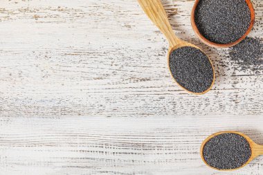 Hafif ahşap arka planda haşhaş tohumlu kase ve kaşıklar.