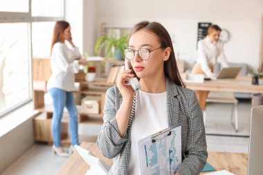 Kadın muhasebeci ofiste telefonla konuşuyor.