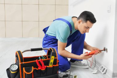 Genç elektrikçi odada voltaj ölçümü yapıyor.