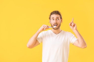 Dişlerini fırçalayan ve arka plandaki bir şeye işaret eden genç bir adam.