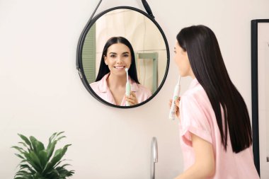 Banyoda dişlerini fırçalayan genç bir kadın.