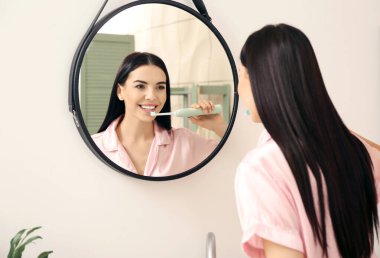 Banyoda dişlerini fırçalayan genç bir kadın.