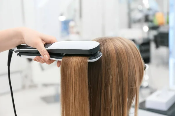 Female hairdresser straightening hair of client in beauty salon, closeup