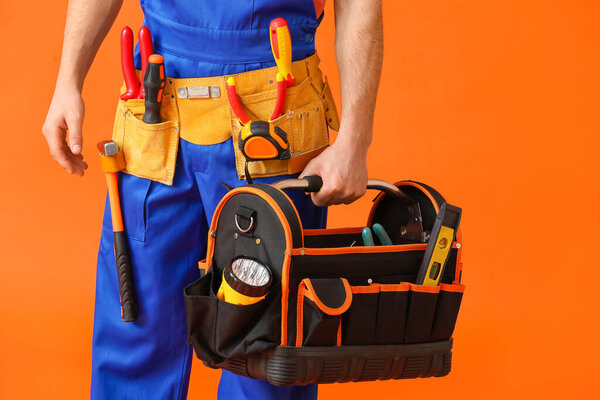 Young electrician with tools on color background, closeup