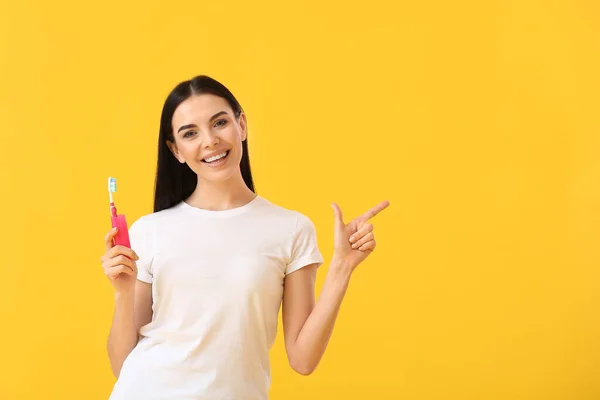歯ブラシを持つ若い女性が何かを指している色の背景に — ストック写真