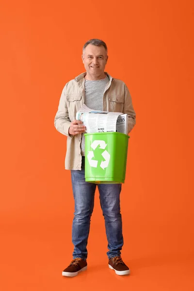 Mature man with newspapers in trash bin on color background. Recycling concept