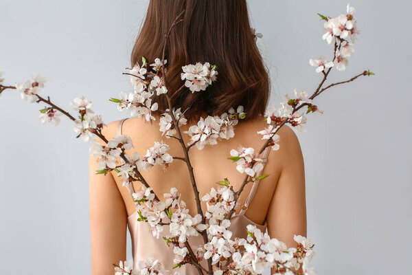 Beautiful young woman with blooming spring branches on grey background