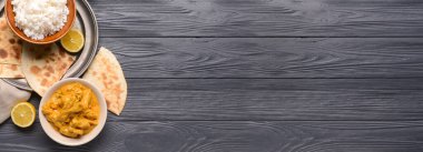 Tabaklar dolusu lezzetli tavuk tikka masala ve ahşap zemin üzerinde pirinç ve metin için yer var.