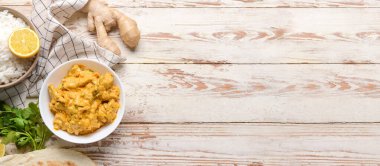 Beyaz ahşap zemin üzerinde bir kase leziz tavuk tikka masala ve metin için yer var.