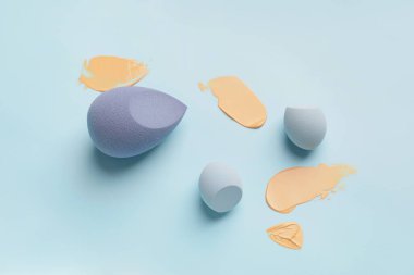 Makeup sponges with samples of tonal foundation on color background clipart