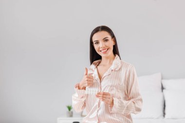 Hapları olan güzel genç bir kadın evde baş parmağını kaldırıyor.