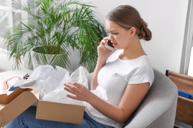 Evde cep telefonuyla konuşan üzgün genç bir kadın.