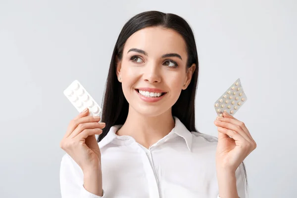 Beautiful young woman with pills on light background