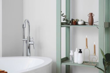 Rafta kozmetik şişeler ve banyoda mumlar var.