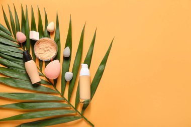 Farklı dekoratif kozmetik ürünleri olan tropikal yaprak ve renk arka planında makyaj süngeri