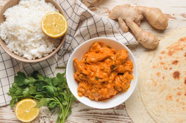 Bir kase lezzetli tavuk tikka masala ve beyaz ahşap arka planda pirinç.