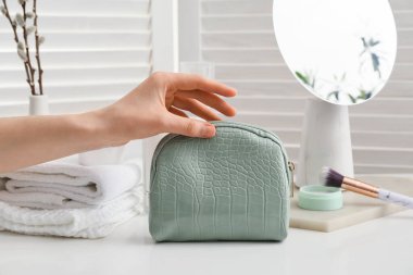 Şık çantalı ve dekoratif kozmetik ürünleri olan bir kadın eli.