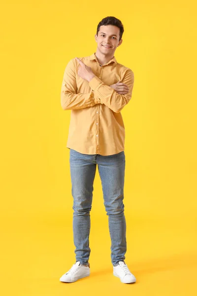 Yakışıklı Genç Adam Sarı Arka Planda Bir Şeye Işaret Ediyor — Stok fotoğraf