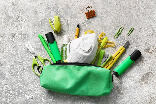 Pencil case with stationery and respirator on grunge background