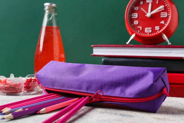 Pencil case with stationery on table near blackboard