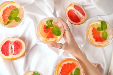Kumaş arka planında bir bardak lezzetli greyfurt kokteyli olan bir kadın eli.