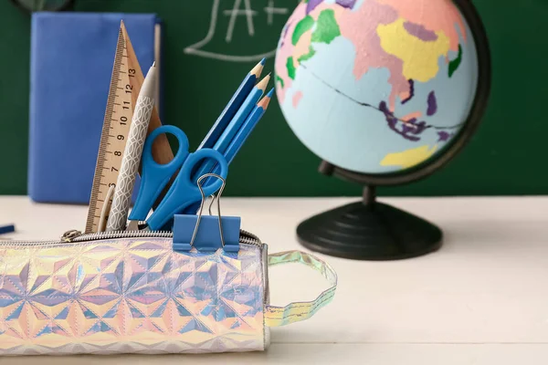 Pencil case and stationery on table near blackboard