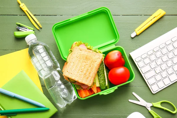 Lunch box with tasty food and school stationery on wooden background