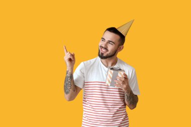 Mutlu genç adam hediye kutusuyla arka plandaki bir şeyi işaret ediyor.