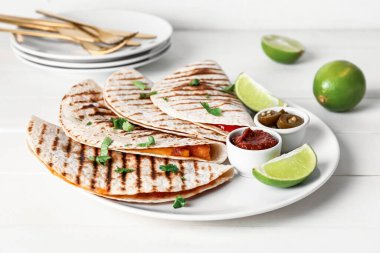 Hafif arkaplanda lezzetli quesadilla, limon, sos ve turşulu jalapeno tabağı