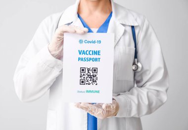 Gri arka planda bağışıklık pasaportu olan doktor, yakın plan.