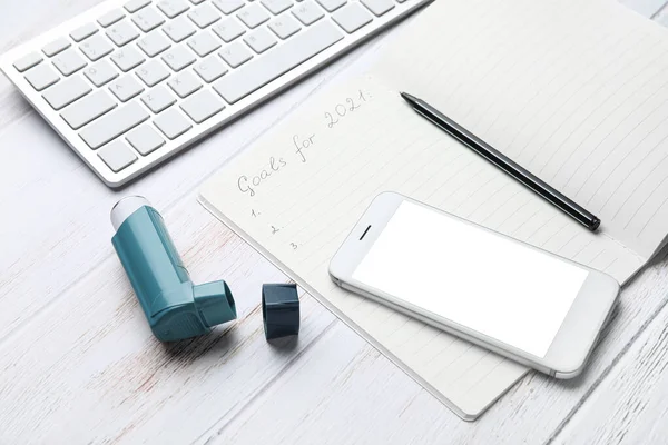 Composition with inhaler, notebook and mobile phone on light wooden background