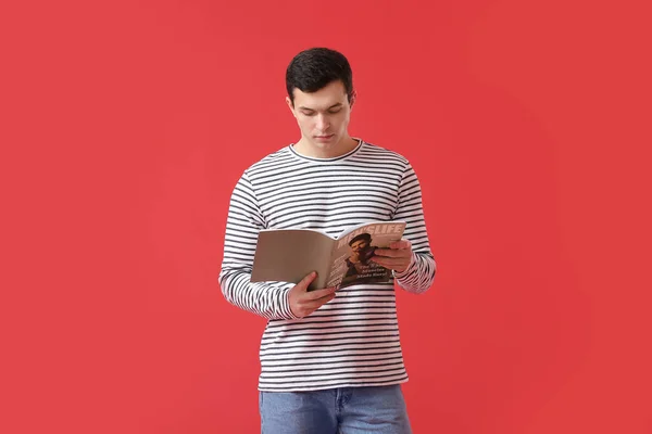 Handsome young man reading magazine on color background