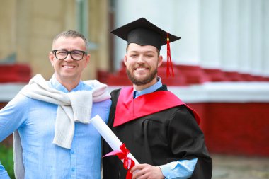 Mezuniyet gününde babasının yanında mutlu bir genç adam.