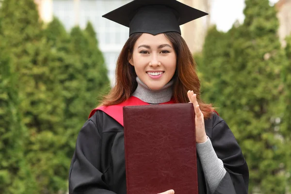 Female student in bachelor robe and with book on her graduation day