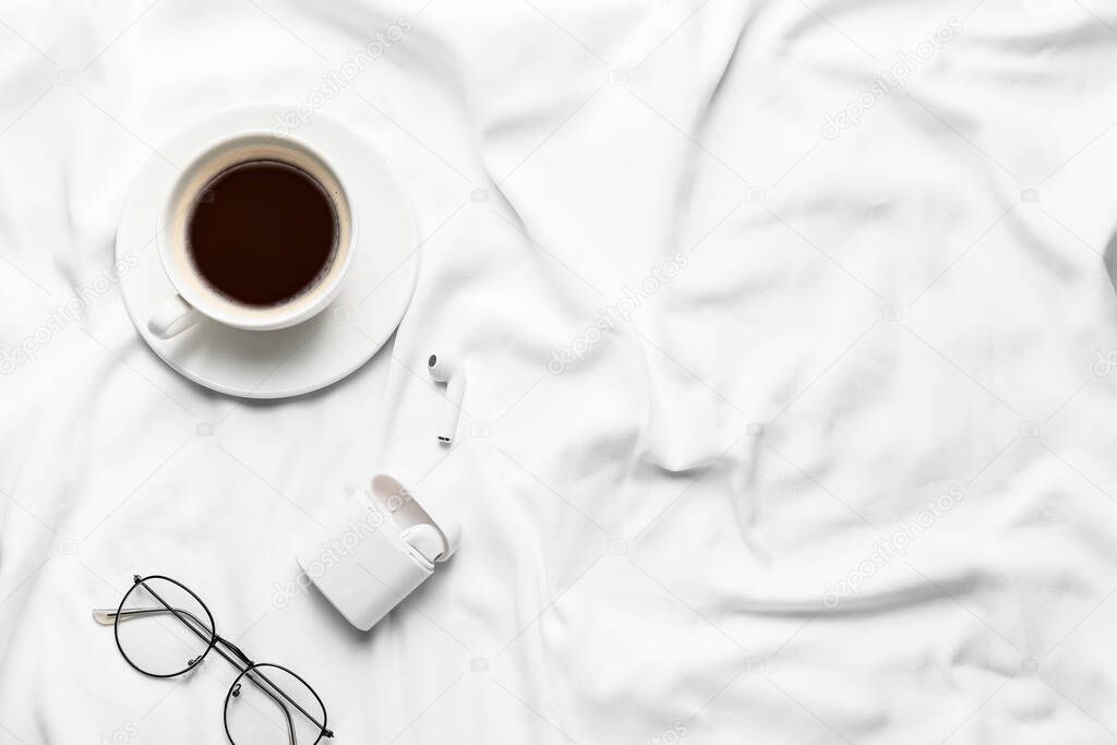 Cup of coffee with earphones and glasses on bed
