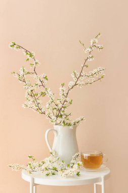 Bir fincan lezzetli çay ve sürahi. Renk duvarının yanındaki masada çiçek açan dallar.