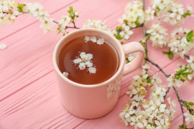 Lezzetli çay bardağı ve renkli ahşap arka planda çiçek açan dallar.