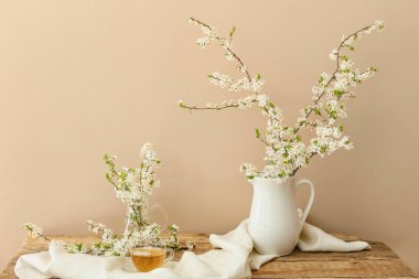 Lezzetli çay fincanı ve tahta masanın üzerinde çiçek açan dalları olan sürahi.