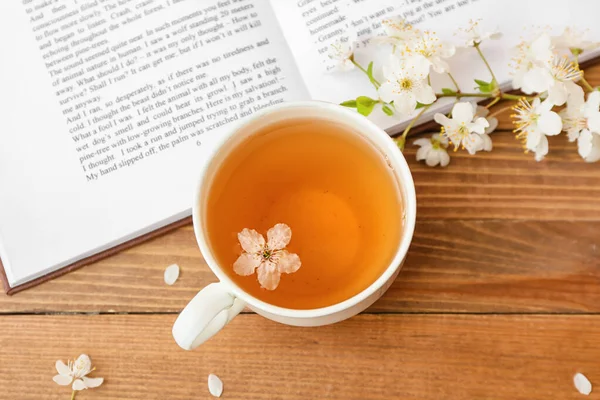 Lezzetli çay, kitap ve ağaç arka planda çiçek açan dallarla dolu bir fincan.