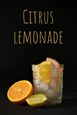 Bir bardak lezzetli soğuk limonata ve koyu arkaplanda narenciye meyvesi.