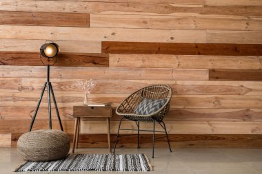 Ahşap duvarın yanında masası ve parlayan lambası olan hasır bir koltuk.