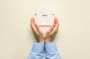 Hafif arka planda kadın eli ve ev figürü