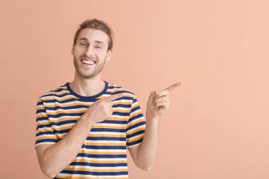 Gülümseyen genç adam arka plandaki bir şeye işaret ediyor.