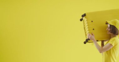 Sarı arka planda bavulu olan genç bir kadın.